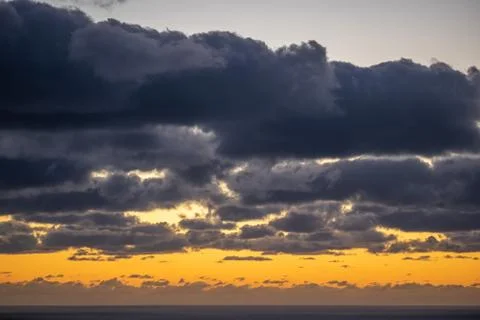 Aerial view of dark clouds back-lit by orange evening light over Tasman sea h Stock Photos