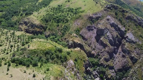 Aerial view of dark volcanic rock peak and terraced orchards in Kazakhstan Видео 337676419