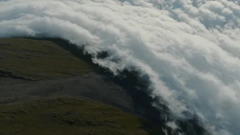 Aerial view of a dense blanket of clouds spilling over the rugged, dark volcanic Stockbeeldmateriaal 335726693