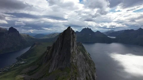 Aerial view of dramatic mountain peak above fjord with clouds and sunlight Stock Footage 343539384