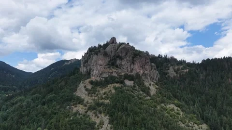 Aerial view of a dramatic rocky cliff peak surrounded by green forest under clou Video stock 341735666