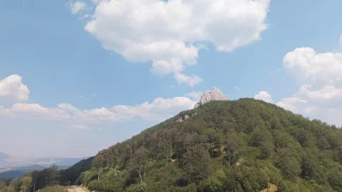 Aerial View of Drone Approaching Forested Hill with Rocky Peak Under Blue Sky Vídeo Stock 342715889