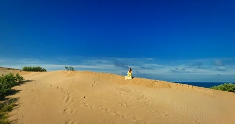 AERIAL View from a drone flying next to a happy woman in a dress on the dunes in Video stock 126899564