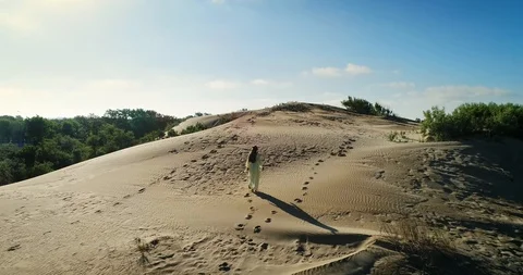 AERIAL View from a drone flying next to a happy woman in a dress on the dunes in Video stock 126899703