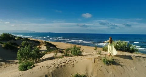 AERIAL View from a drone flying next to a happy woman in a dress on the dunes in Video stock 126900366