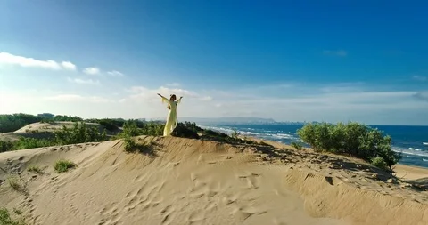 AERIAL View from a drone flying next to a happy woman in a dress on the dunes in Video stock 126900604