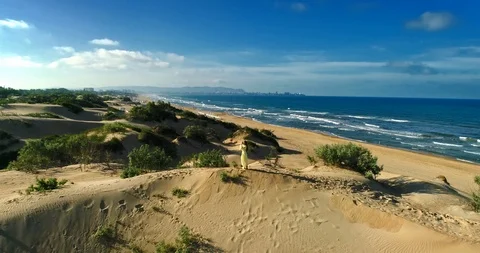 AERIAL View from a drone flying next to a happy woman in a dress on the dunes in Video stock 126901069