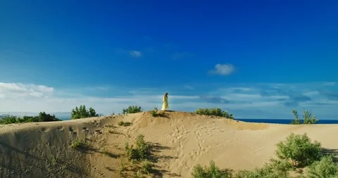 AERIAL View from a drone flying next to a happy woman in a dress on the dunes in Video stock 126901258