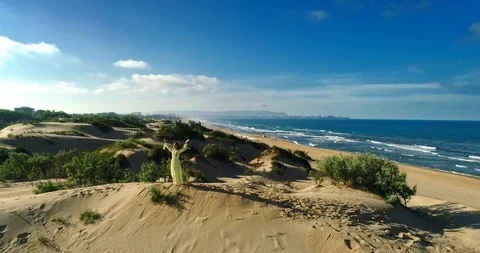 AERIAL View from a drone flying next to a happy woman in a dress on the dunes in Video stock 126901463