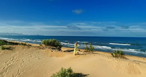 AERIAL View from a drone flying next to a happy woman in a dress on the dunes in Video stock 126901748