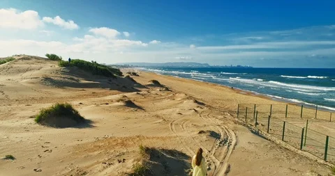 AERIAL View from a drone flying next to a happy woman in a dress on the dunes in Video stock 126909016