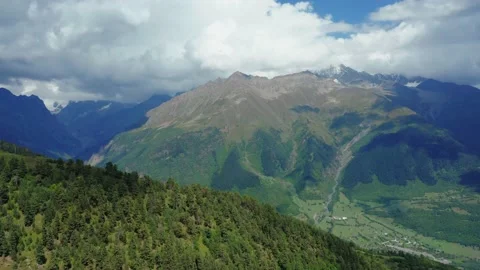 Aerial view from a drone on the forest against mountains and cloudy blue sky. Stock Footage 163102575