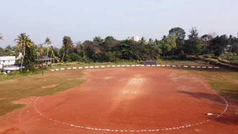 Aerial view of empty cricket ground with red clay pitch and green trees in Stock Footage 327338182