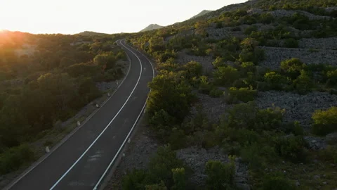Aerial view of empty winding mountain road through rocky hills at sunset Stock Footage 346000652