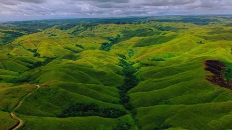 Aerial view of endless green rolling hills and lush valleys under a cloudy sky Stock Footage 339781565