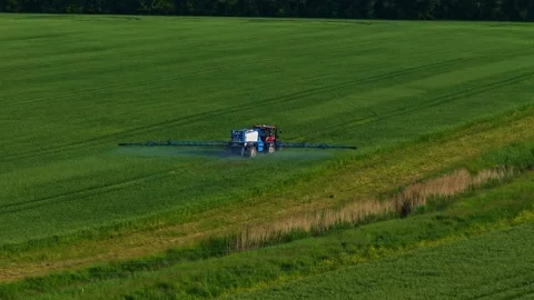 Aerial view of a farm sprayer working across a green crop field, applying Stock Footage 334000682
