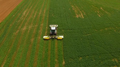 Aerial view of a farmer in a modern tractor mowing a green fresh grass field. Stock Footage 89433367