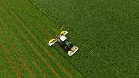 Aerial view of a farmer in a modern tractor mowing a green fresh grass field. Stock Footage 89439992