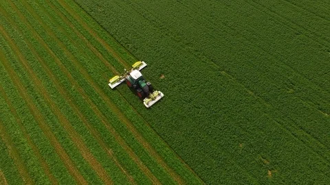Aerial view of a farmer in a modern tractor mowing a green fresh grass field. Stock Footage 89440846