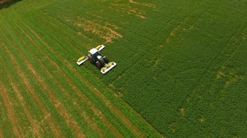 Aerial view of a farmer in a modern tractor mowing a green fresh grass field. Stock Footage 89472684