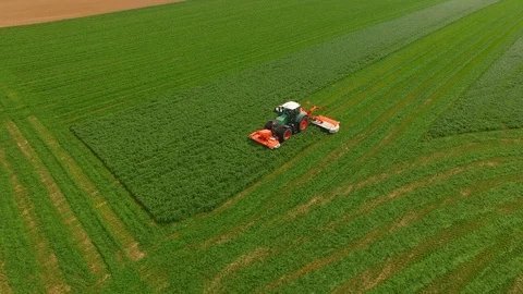 Aerial view of a farmer in a modern tractor mowing a green fresh grass field. Stock Footage 89515505
