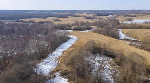 Aerial view of fields with copse, dry yellow grass, a stream, remnants of sno Stock Photos