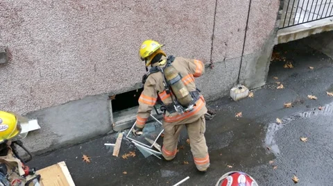 Aerial view of firemen opening up basement windows with smoke showing Vidéo 43543074