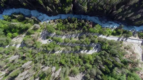 Aerial view flight over a winding mountain road on the banks of a stormy river. Stock Footage 156347041