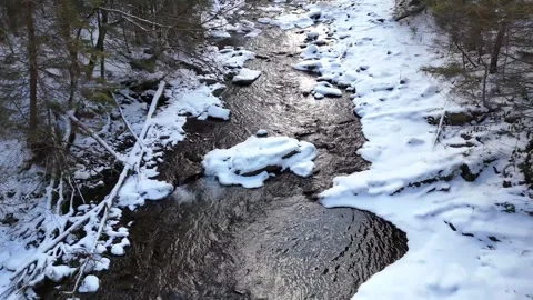Aerial view of flowing stream through snow-covered landscape showcasing the Stock Footage 335886194
