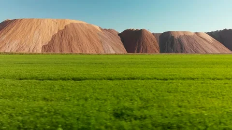 Aerial view fly sideways under green field with potash waste mountains Stock Footage 170551027