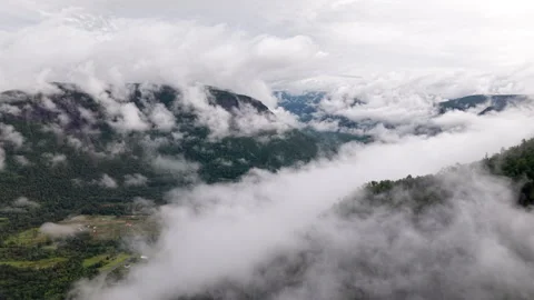 Aerial view flying above low clouds and fog revealing green valley and Stock Footage 345676979