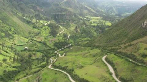 Aerial view flying backwards over a in grass coved green valley with dirt roads Stock Footage 142752732