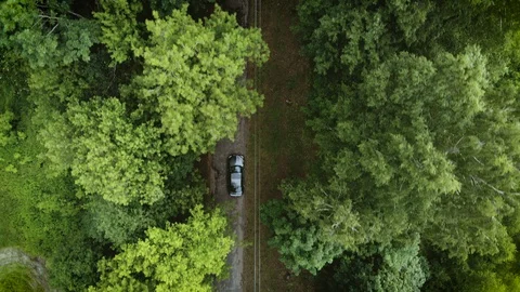 Aerial view flying over old patched two lane forest road with car Stock Footage 129452145