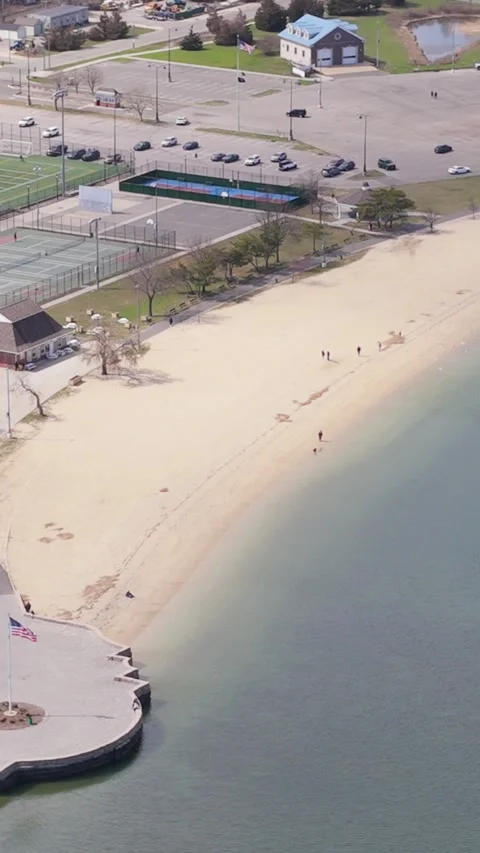 Aerial view flying over a sandy beach, tennis courts, and parking lot on long Stock-Footage 333161333