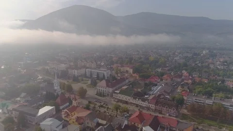 Aerial View: Flying over the small city covered by clouds. Aerial camera shot Видео 103265431
