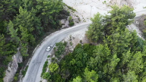 Aerial view flying over two lane forest road with car moving green trees Stock Footage 130450207