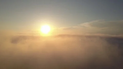 Aerial view flying through clouds and mist with sun in the distance Stock Footage 77062715