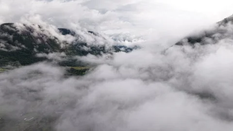 Aerial view flying through thick white fog and clouds covering mountain valley Stock Footage 345679530