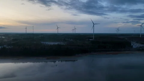 Aerial view flying toward wind turbines rotating near lake at sunset Stock Footage 295913035
