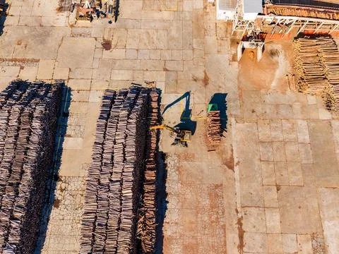 Aerial view of a forklift moving timber stacks across a paved lumber yard d.. 스톡 사진