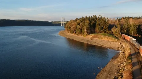 Aerial view of a freight train with blue water and distant bridge Video stock 101861698
