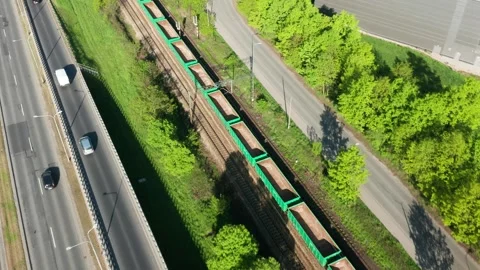Aerial view of freight train with green wagons and cars on highway in spring Stock Footage 308646328