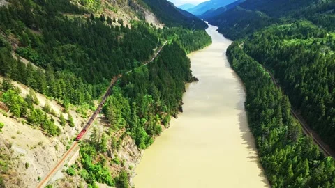 Aerial view of a freight train moving along a river in a canyon Stock Footage 343543448