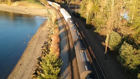 Aerial view of a freight train passing below next to rocky beach and blue water Video stock 101861627