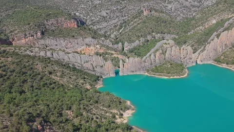 Aerial view of a great rock wall rising from a turquoise lake 스톡 동영상 343325477