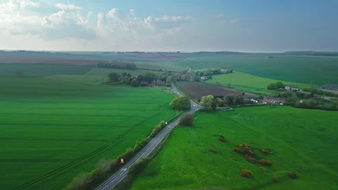 Aerial view of green fields with a winding road and distant village Vídeo Stock 346853963