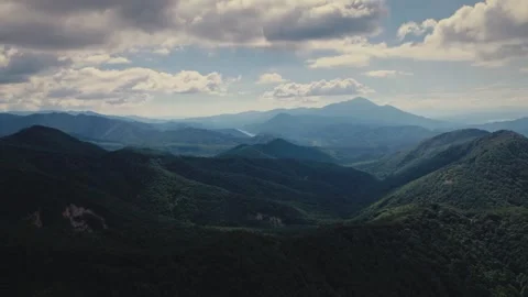 Aerial view of green forest valley and mountain range under cloudy sky Stock Footage 345833360