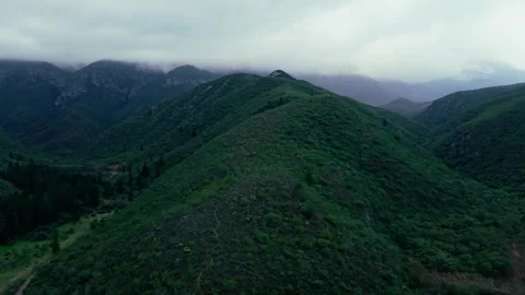 Aerial view of green mountain slopes descending to a valley dam Stock Footage 342334707