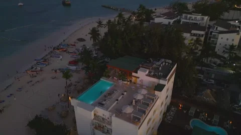 Aerial view of a hotel with a rooftop pool illuminated at dusk on the beach Stock Footage 306334488