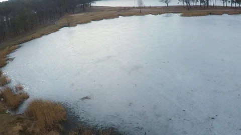 Aerial view of an ice lake in a pine forest with a sandy beach in early spring Stock Footage 104160752